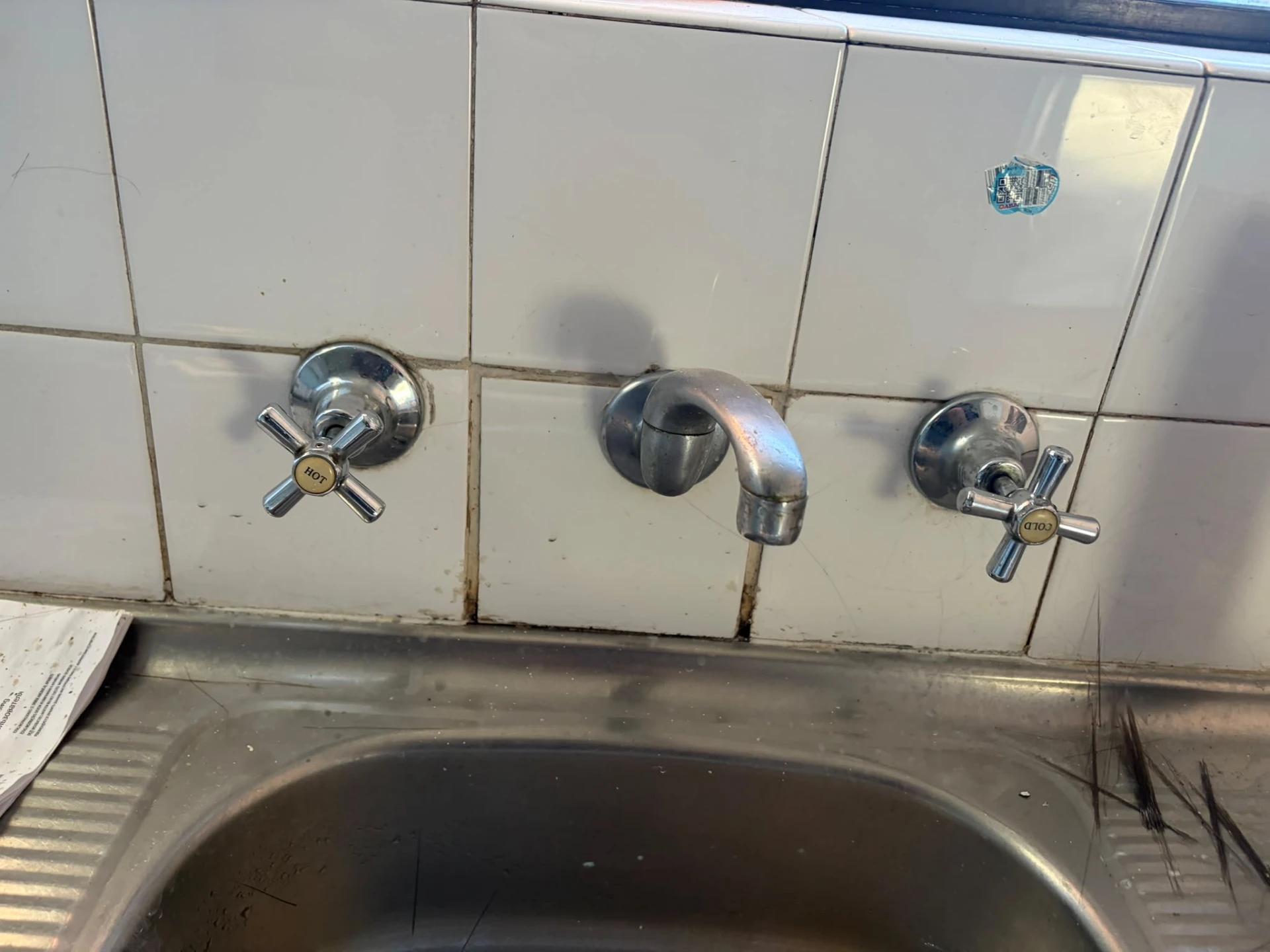 Old worn laundry taps over a stainless steel laundry trough before repair